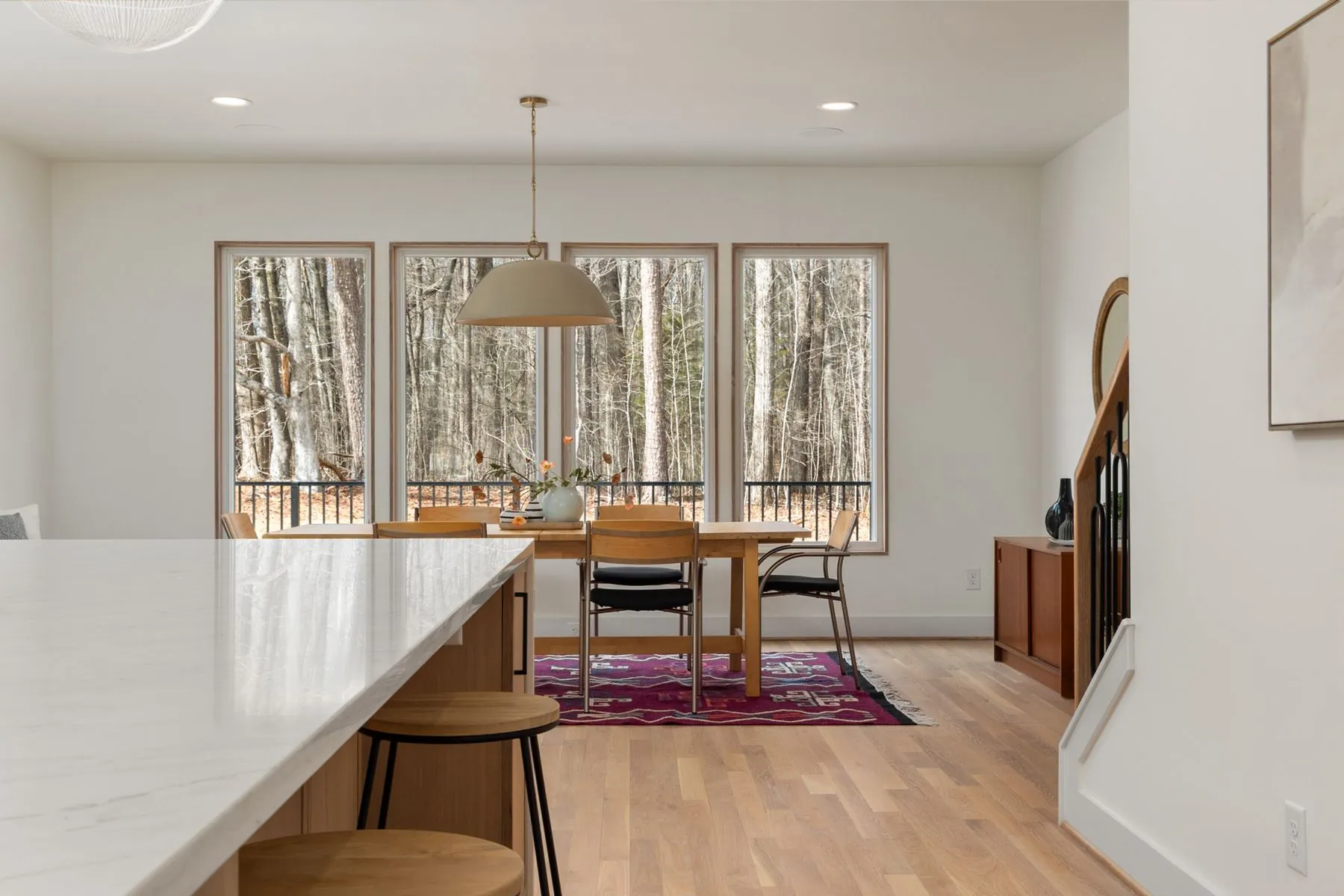 A dining room with a long table and tall windows onto trees
