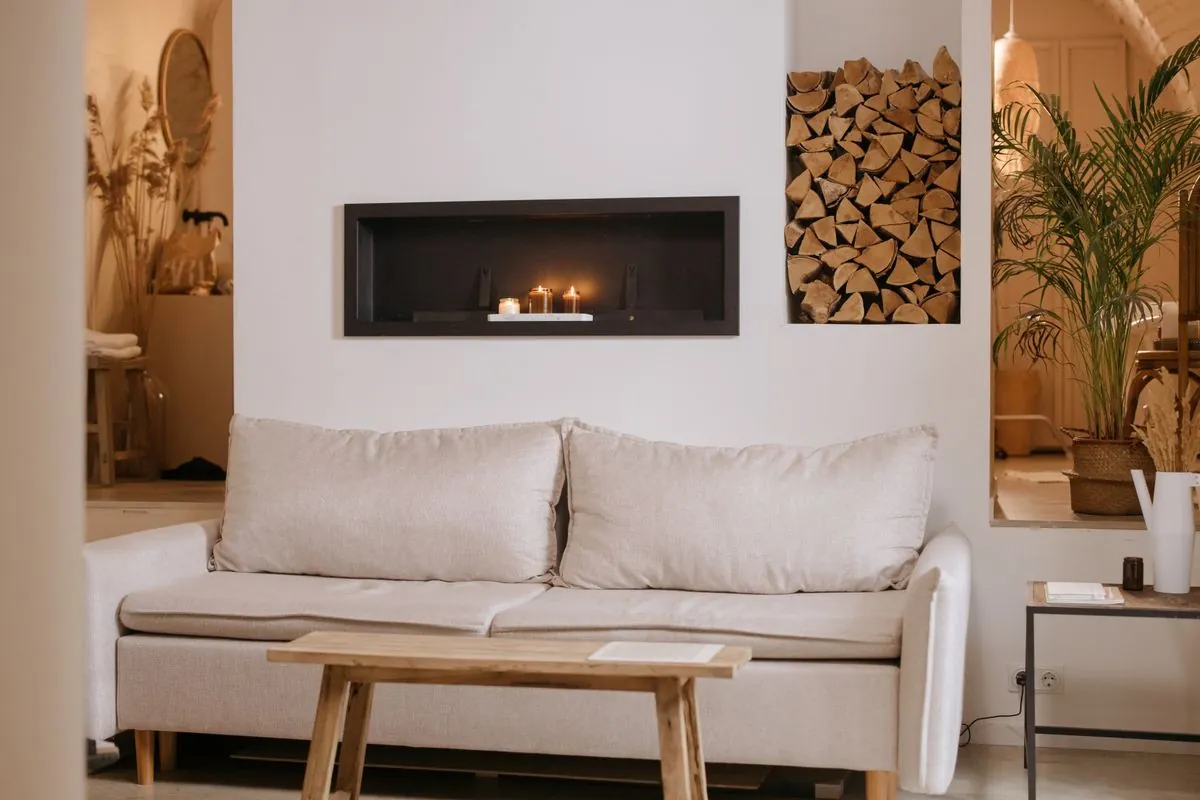 A pale sofa beside a lit fireplace and stacked logs