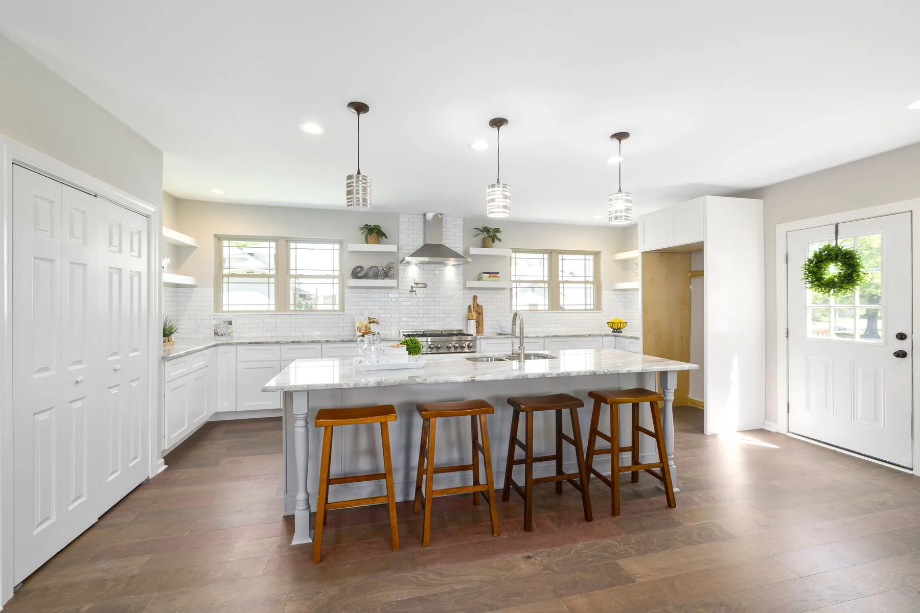 A white kitchen with a marble island under three pendant lights